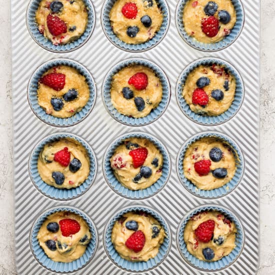 A muffin tin filled with muffins and berries.