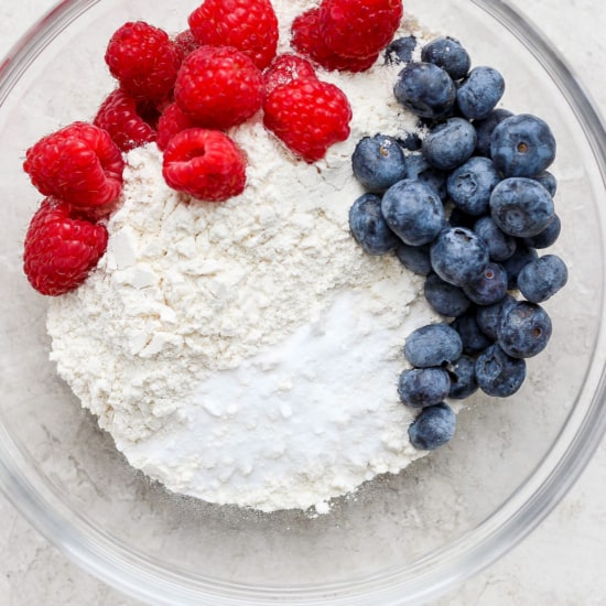 A bowl with flour, berries and blueberries.