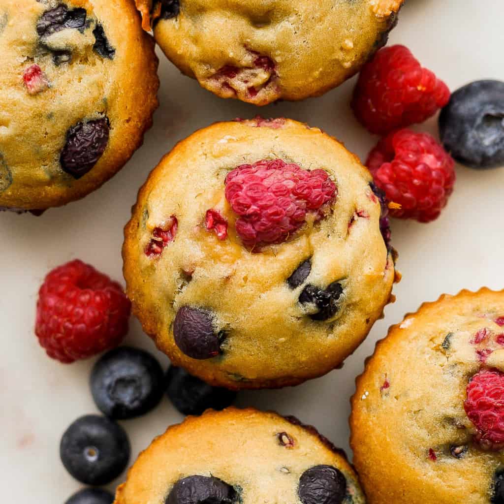 A group of muffins with raspberries and blueberries.
