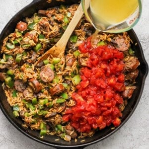 A person pouring oil into a skillet with rice and sausage.