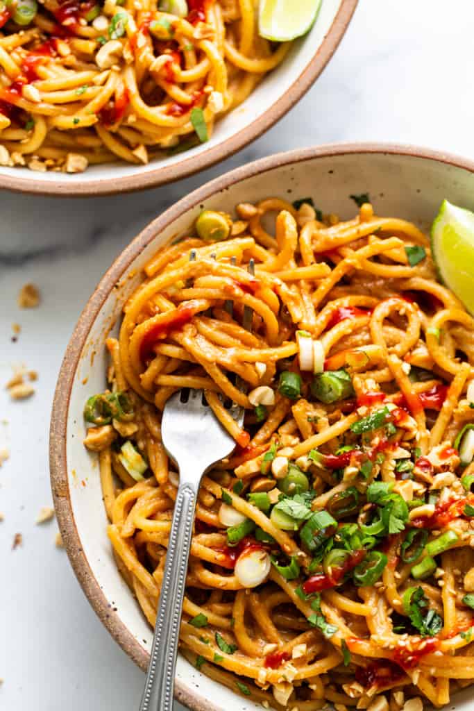Two bowls of noodles with peanut sauce and lime.