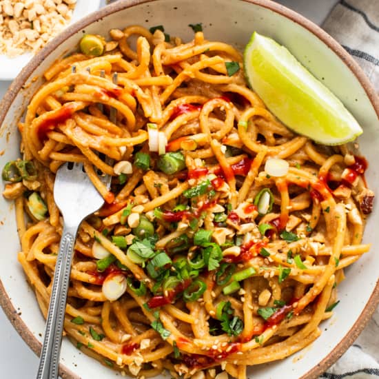 Thai peanut noodles in a bowl with lime and peanuts.