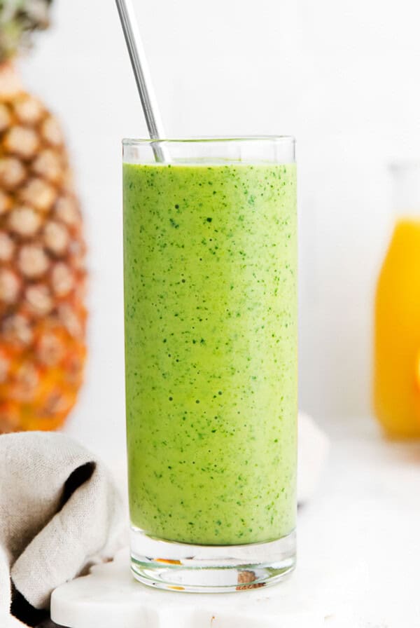 A glass with a green spinach smoothie and a spoon.