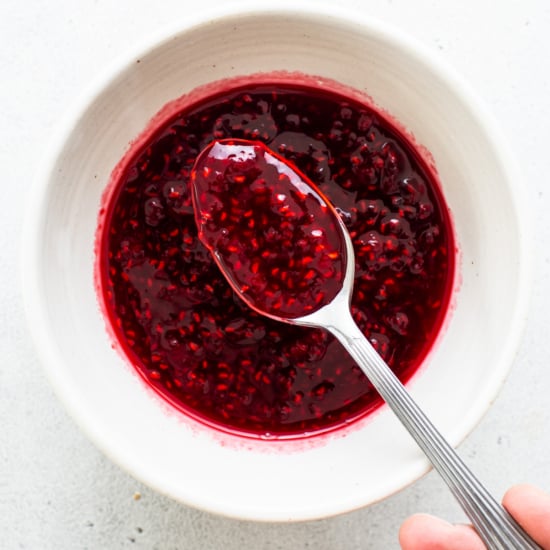 Raspberry jam in a white bowl with a spoon.