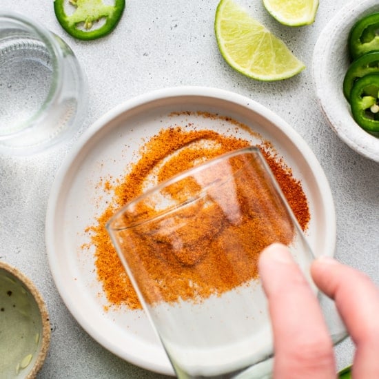 A person sprinkling salt on a glass with limes and jalapenos.