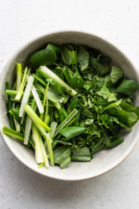 Fresh herbs in a bowl on a white surface.