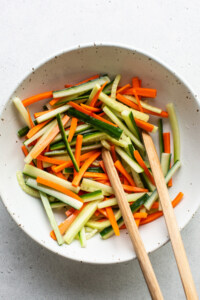 A white bowl with carrots and cucumbers in it.