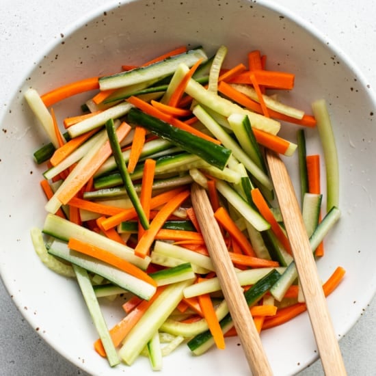 A white bowl with carrots and cucumbers in it.