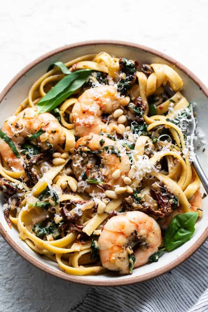 A bowl of pasta with shrimp, mushrooms and spinach.