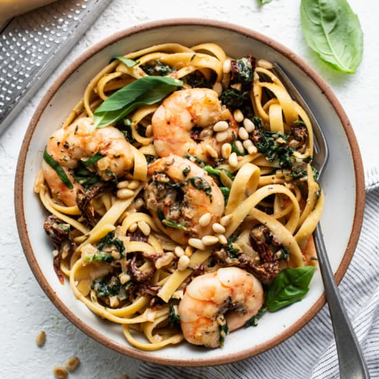 A bowl of pasta with shrimp and basil.