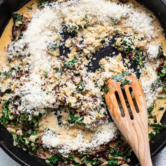 A skillet filled with spinach and cheese with a wooden spoon.