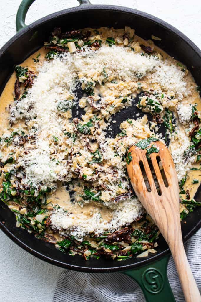 A skillet filled with spinach and cheese with a wooden spoon.