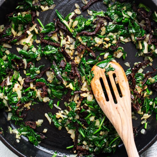 A skillet filled with greens and a wooden spoon.