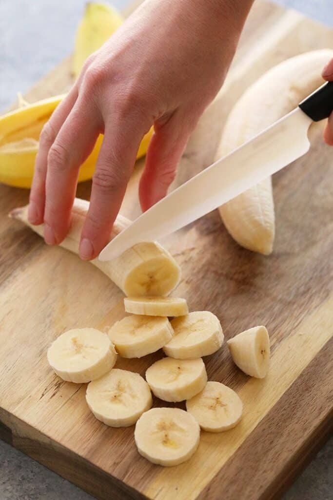 Slicing a banana for nice cream on a wooden cutting board.