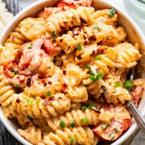 A bowl of creamy baked macaroni and cheese with sliced tomatoes and chopped green onions on top.