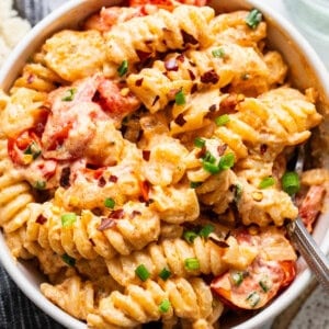 A bowl of creamy pasta with tomato pieces and sprinkled with herbs.