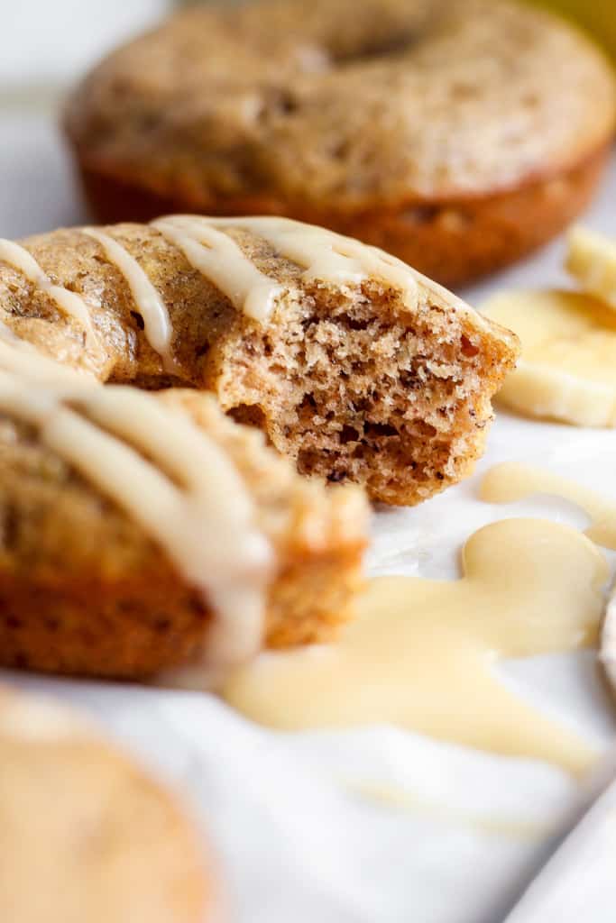 Close-up of a partially eaten muffin with white glaze on top, with more muffins and banana slices blurred in the background.