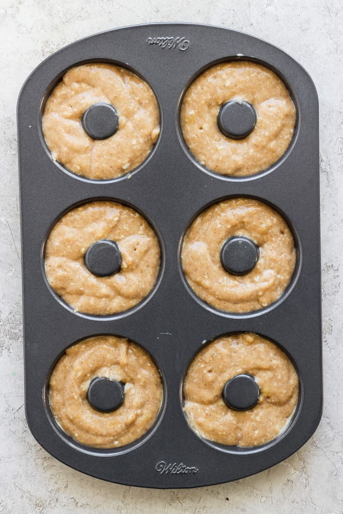 A six-cavity donut baking pan filled with raw donut batter, ready to be baked.