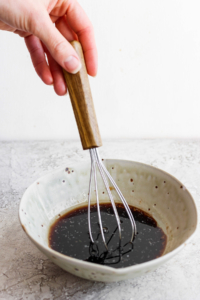 A hand whisking a liquid mixture in a ceramic bowl.