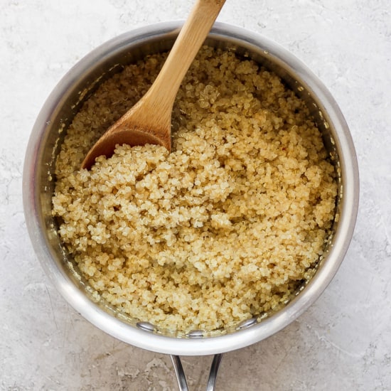 Cooked quinoa in a pot with a wooden spoon.
