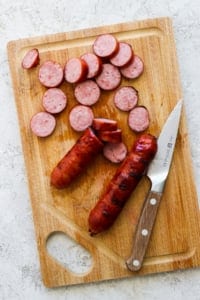 Sliced sausage on a wooden cutting board with a knife.