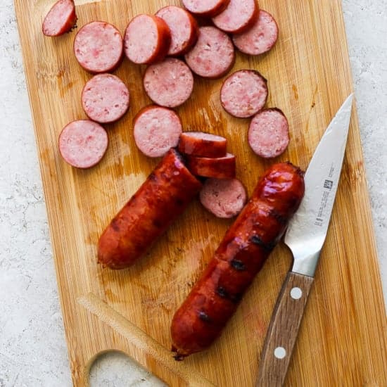Sliced sausage on a wooden cutting board with a knife.