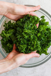 Hands holding fresh kale above a glass bowl.