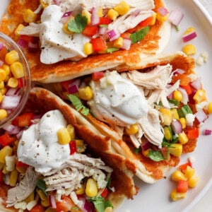 A plate containing chicken tacos garnished with corn, diced tomatoes, red onion, cilantro, and a dollop of sour cream, served on a white surface.