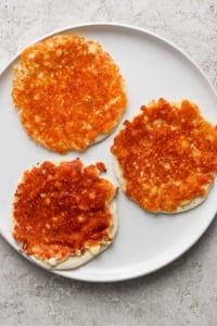 Three golden-brown cheese pancakes on a white plate with a light textured background.