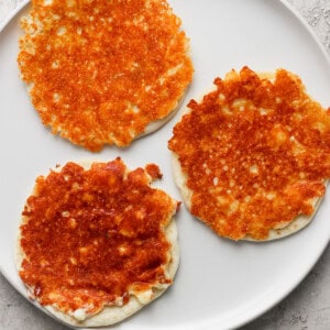 Three golden-brown cheese pancakes on a white plate with a light textured background.