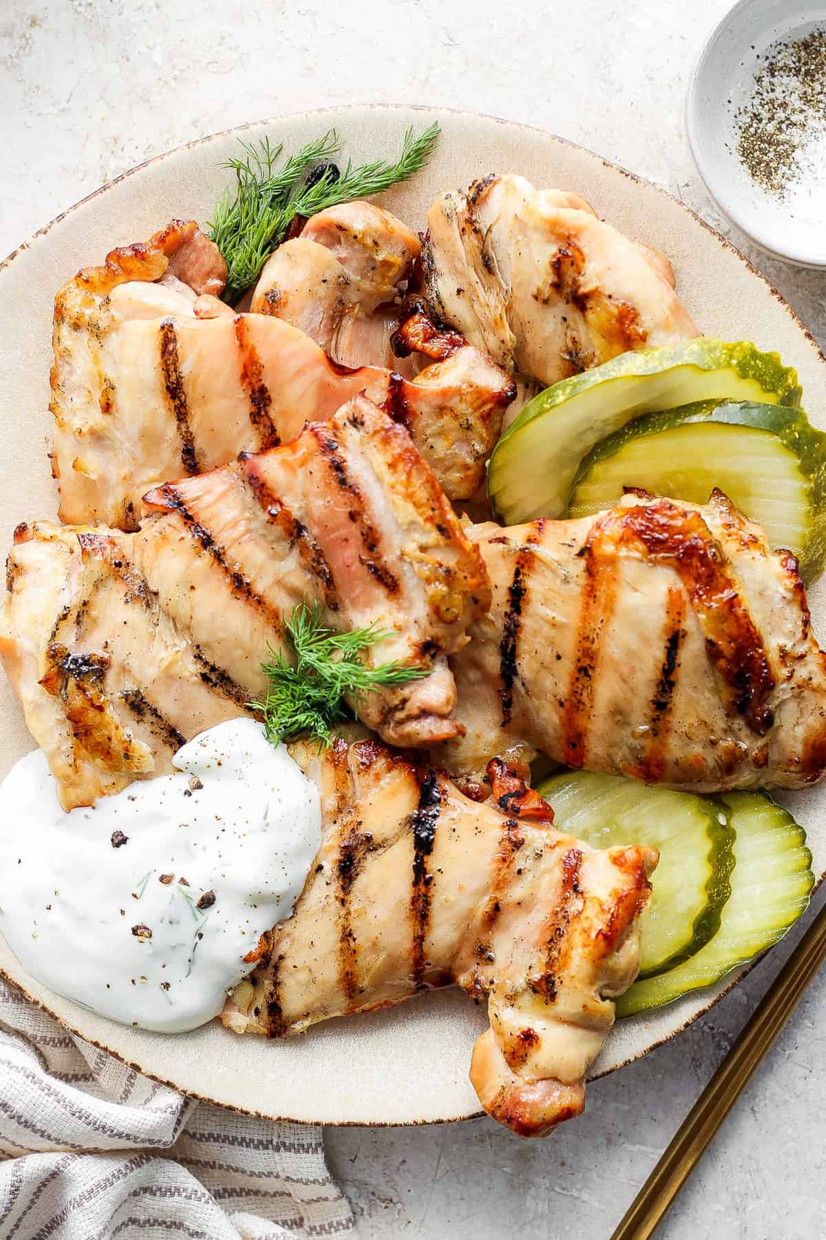 Grilled chicken breasts served with pickles and a dollop of sauce on a plate.