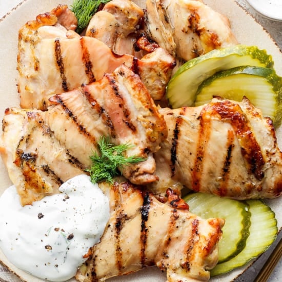 Grilled chicken breast slices served with pickles and a dollop of sour cream on a plate.