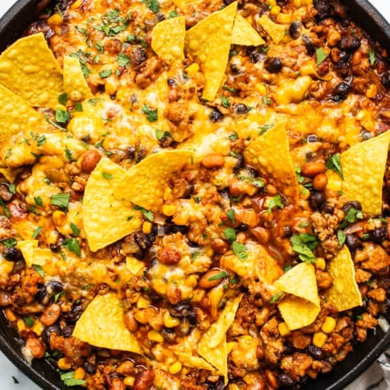 A skillet of baked nachos with melted cheese, ground meat, beans, and corn, garnished with crispy tortilla chips.