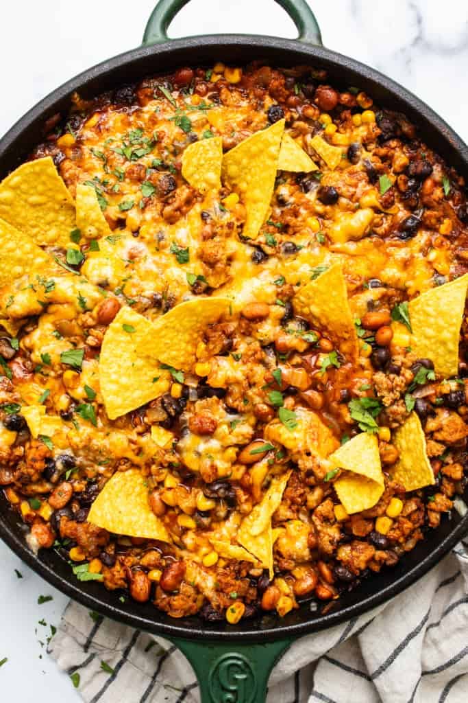 A s،et of baked nac،s with melted cheese, ground meat, beans, and corn, garnished with crispy tortilla chips.