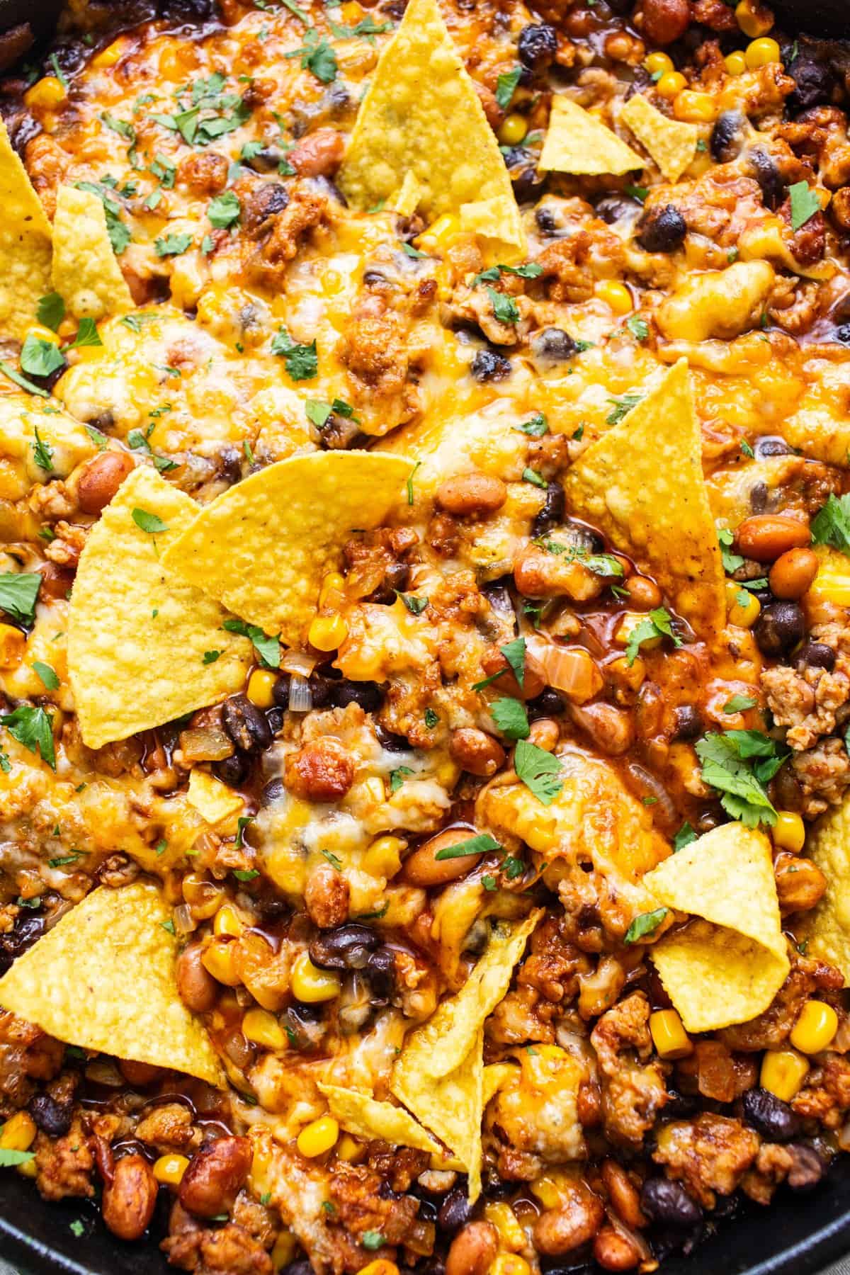 A skillet with nachos covered in melted cheese, ground meat, beans, corn, and garnished with fresh herbs.