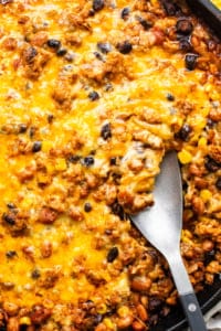 A skillet with baked cheesy casserole containing ground meat, black beans, and corn.
