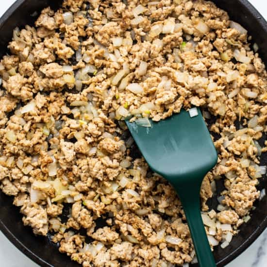 Ground meat cooked with diced onions in a cast iron skillet, with a green spatula.