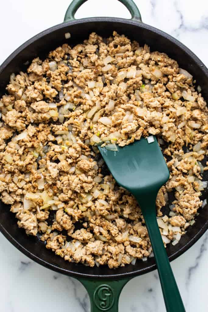 Ground meat cooked with diced onions in a cast iron skillet, with a green spatula.