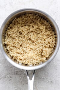 A saucepan filled with cooked grains, possibly quinoa, on a textured surface.