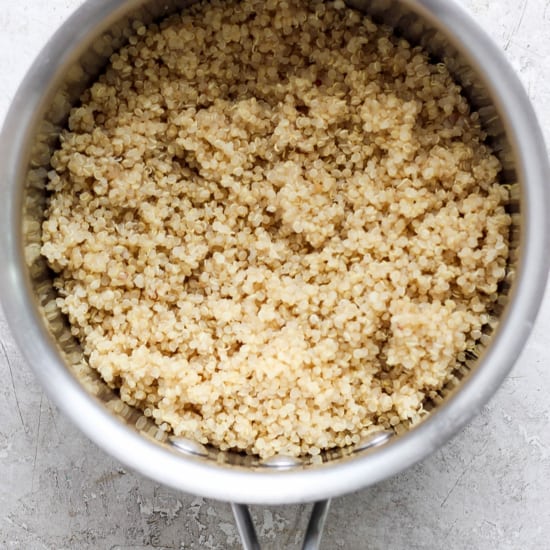 A saucepan filled with cooked grains, possibly quinoa, on a textured surface.