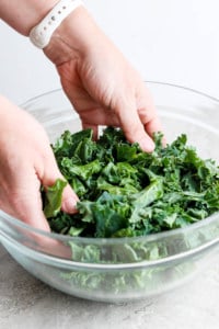 A person is massaging kale in a glass bowl.