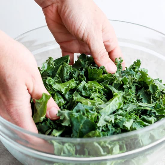 A person is massaging kale in a glass bowl.