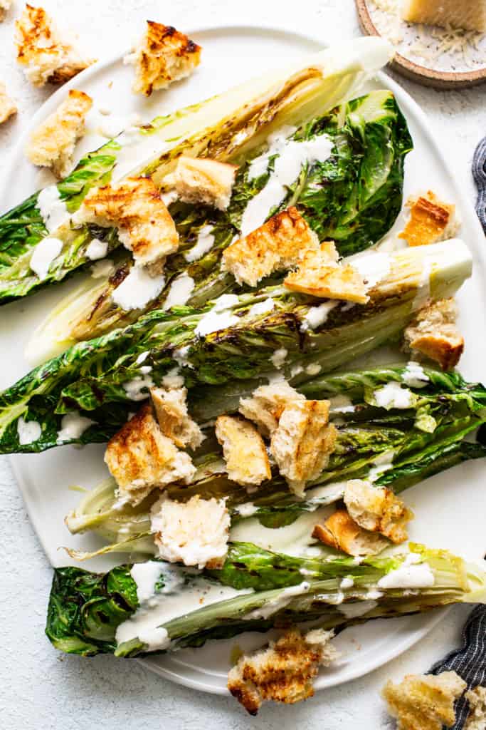 Grilled romaine lettuce topped with croutons and drizzled with creamy dressing on a white plate.
