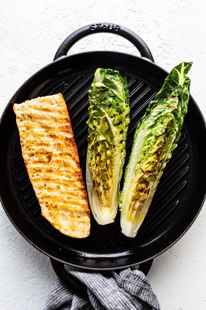 Grilled fish fillet and halves of romaine lettuce on a stove-top grill pan.