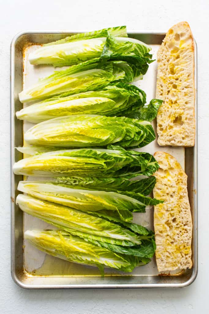 Fresh heads of romaine lettuce and slices of bread arranged on a baking tray.