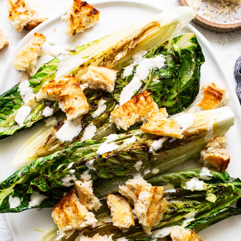 Grilled romaine lettuce with croutons and drizzled dressing connected  a plate.