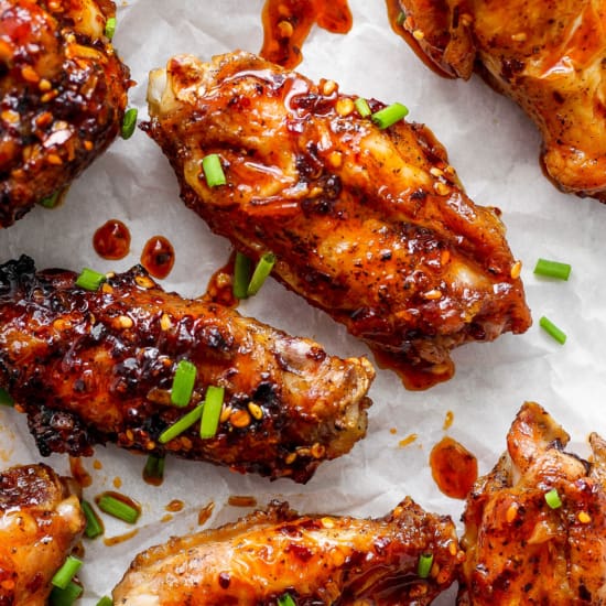 Glazed chicken wings sprinkled with sesame seeds and chopped green onions on parchment paper.