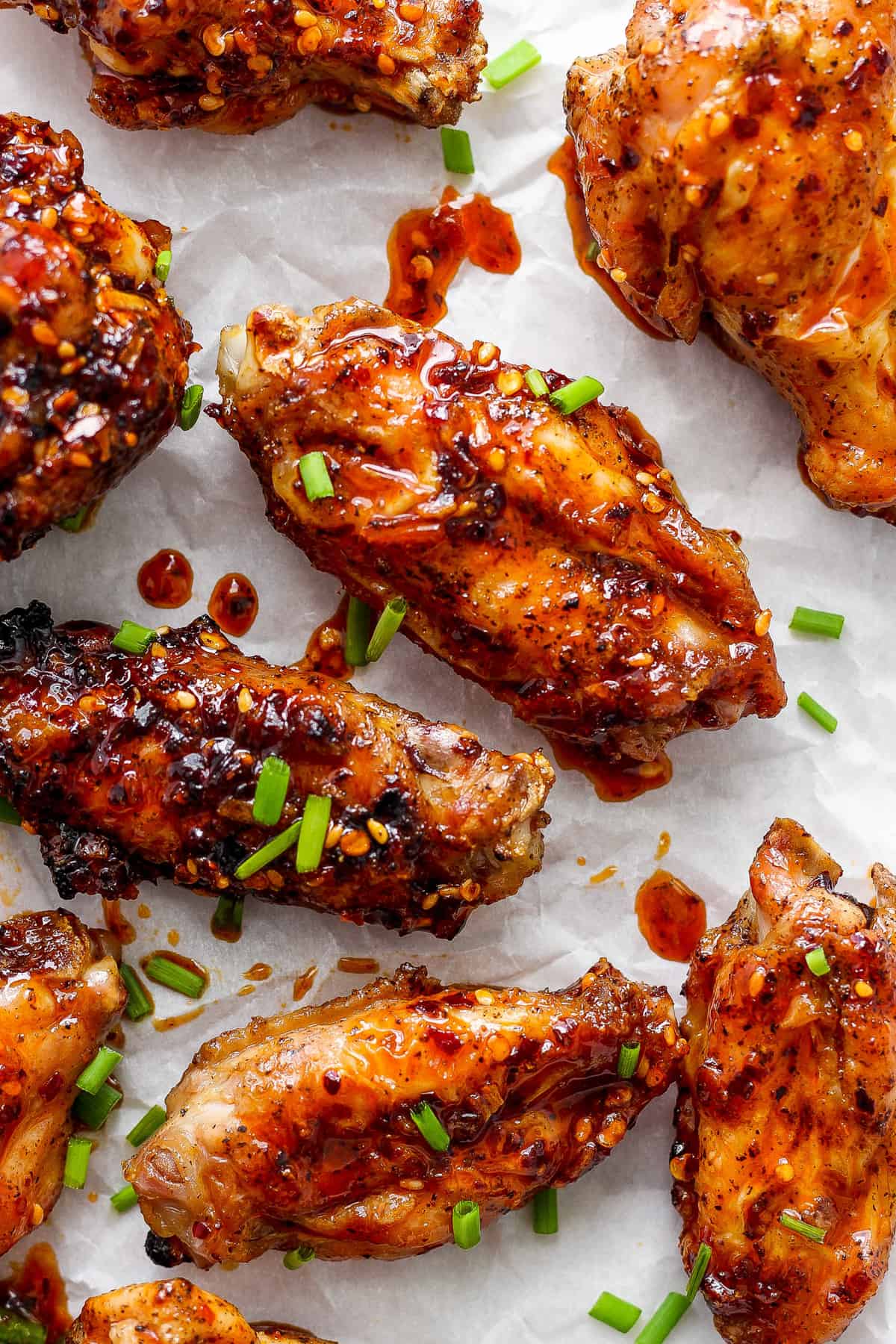 Glazed chicken wings sprinkled with sesame seeds and chopped green onions on parchment paper.