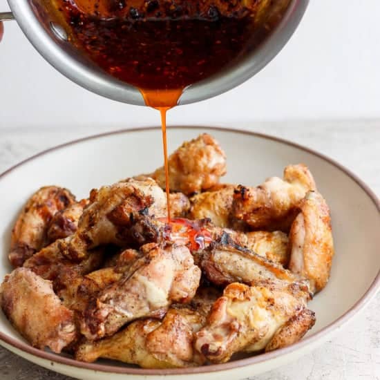 Pouring sauce over a plate of cooked chicken wings.