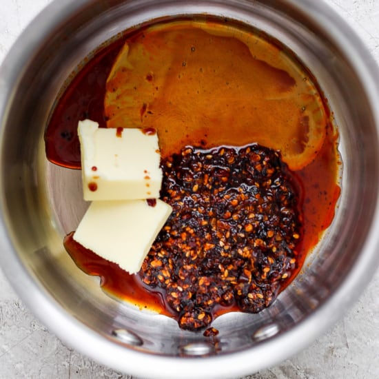 Ingredients in a saucepan including butter, chili flakes, and a dark liquid, possibly soy sauce or vinegar, preparing for a recipe.